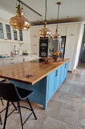 אי מטבח עם ארונות אחסון משני הצדדים בצבע כחול ומשטח בוצ'ר אלון עם תאורה מתאימה מעל האי.